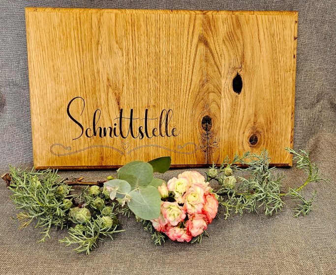 Holztafel mit dem Schriftzug "Schmidtstelle" und einer Blumenarrangement.